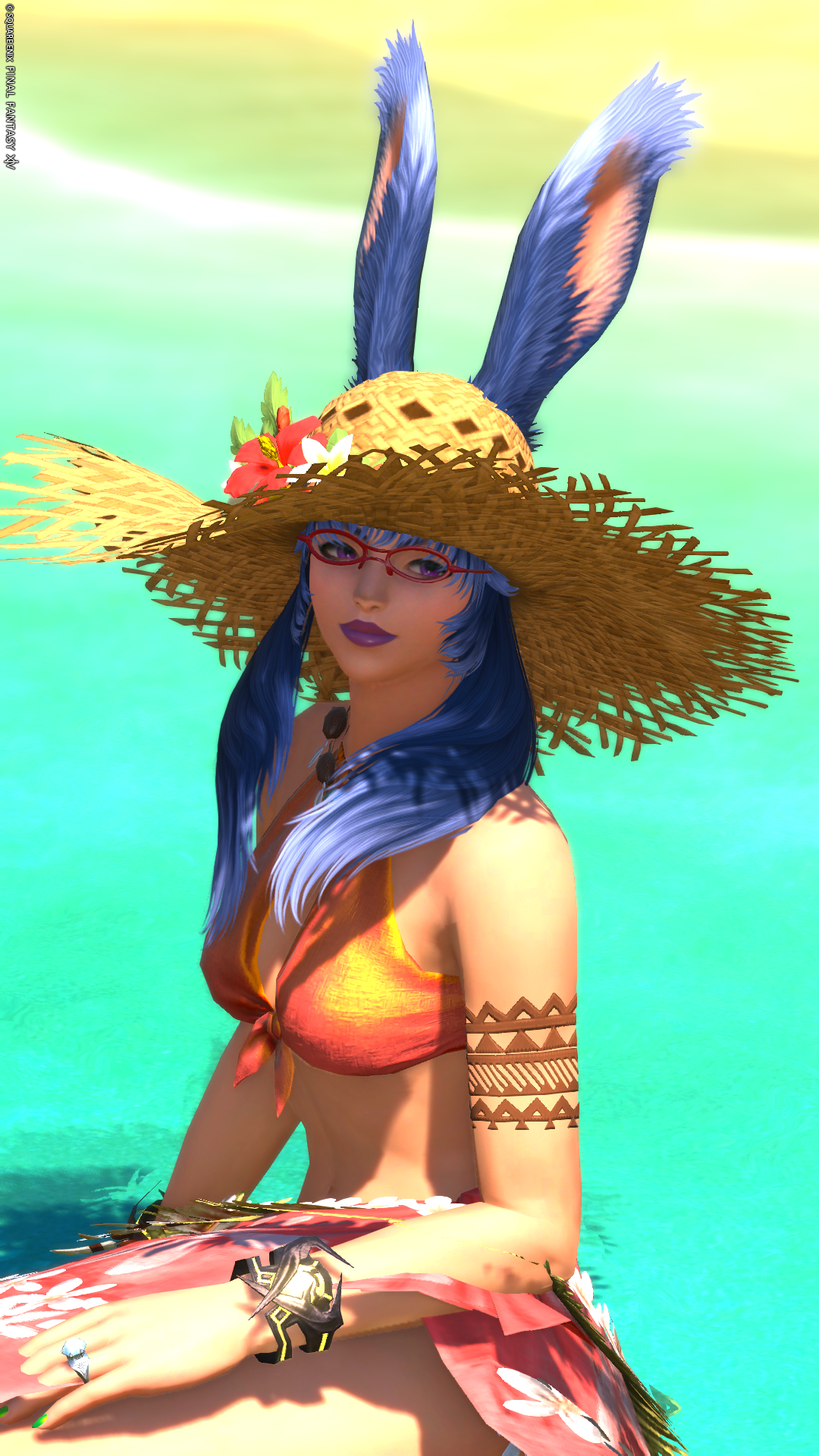 Me wearing beach attire with a large wide-brimmed straw hat sitting in shallow beach water.